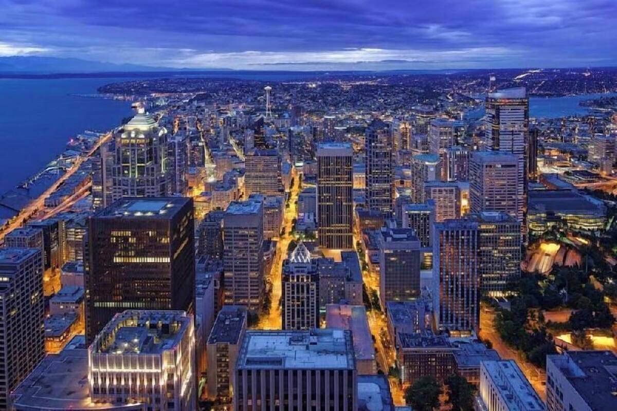 Un paisaje urbano al atardecer con edificios altos, una torre destacada y una zona costera.
