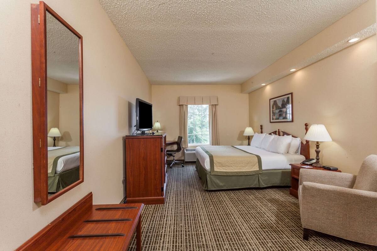 Habitación de hotel con una cama grande, un escritorio con computadora, una silla, un televisor y una ventana con cortinas.