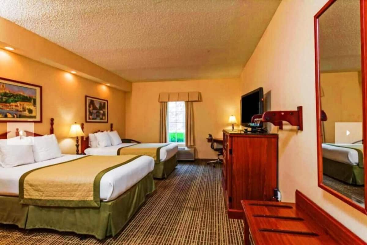 Una habitación de hotel con dos camas, un escritorio, una silla, un televisor y un espejo grande.