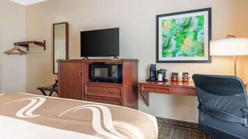 Habitación de hotel con una cama, un escritorio con computadora, microondas, cafetera y un cuadro abstracto en la pared.