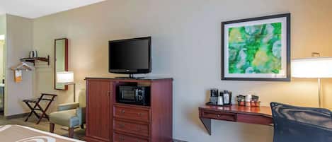 A hotel room with a bed, a TV on a wooden cabinet, a desk with a lamp, a chair, and a painting on the wall.
