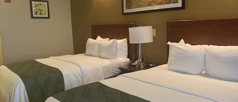 A hotel room with two beds, a nightstand with a lamp, a phone, and a framed picture on the wall.