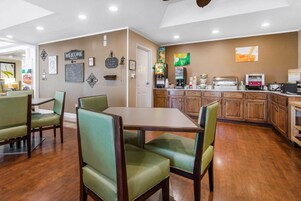 A restaurant with wooden cabinets, a chalkboard menu, and green upholstered chairs.