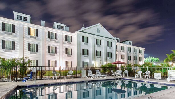 A hotel with a swimming pool, lounge chairs, and a covered area with umbrellas. - Quality Inn Palm Bay - Melbourne I-95 (Palm Bay)
