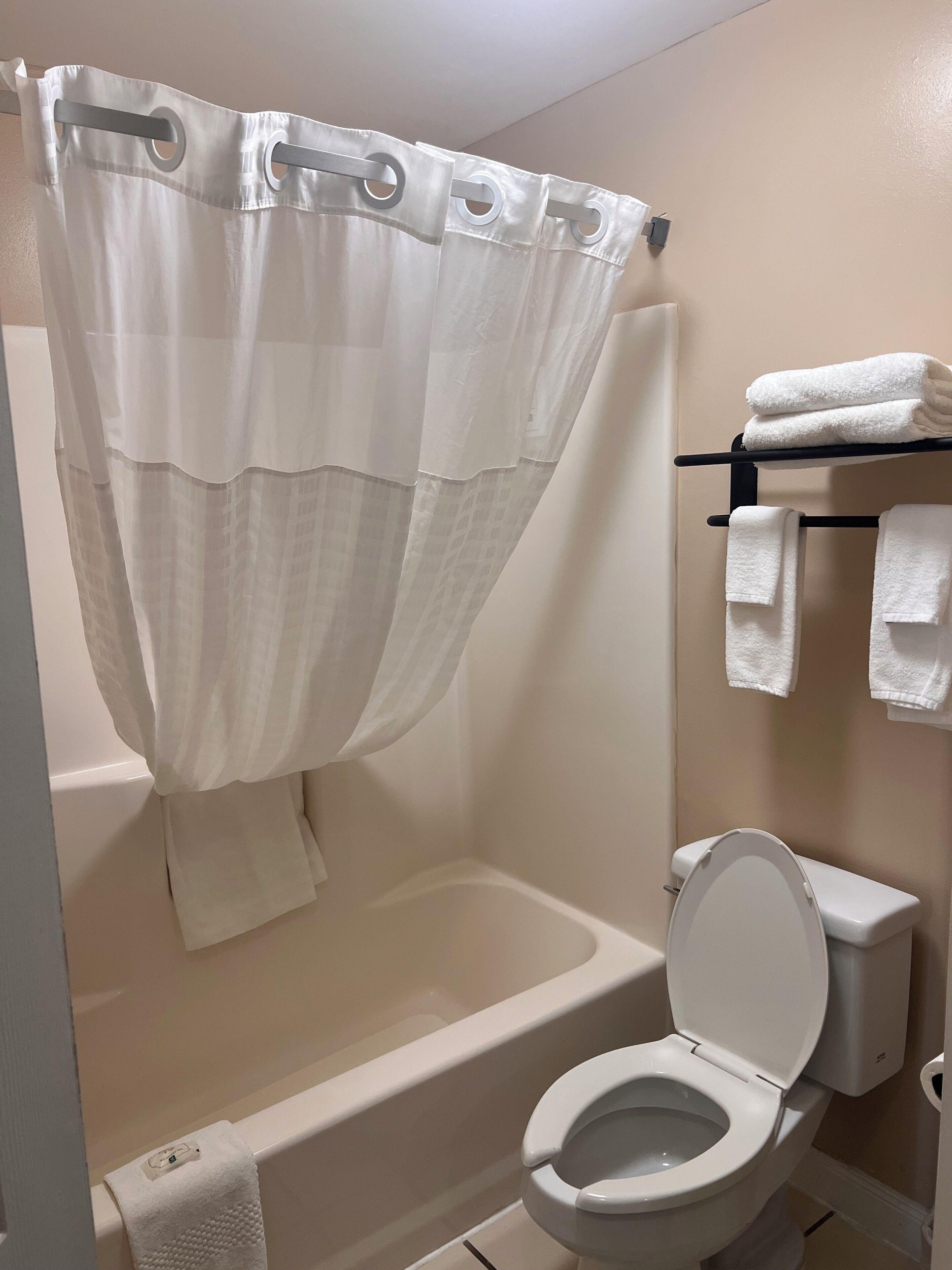 A bathroom with a bathtub, toilet, and a towel rack with folded towels.