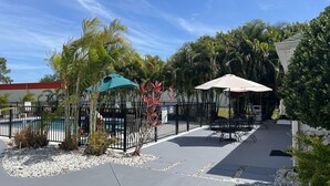 A pool area with a fence, outdoor seating, and palm trees. - Quality Inn Palm Bay - Melbourne I-95 (Palm Bay)