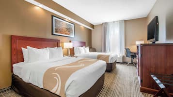 A hotel room with two beds, a desk, a television, and a painting on the wall.