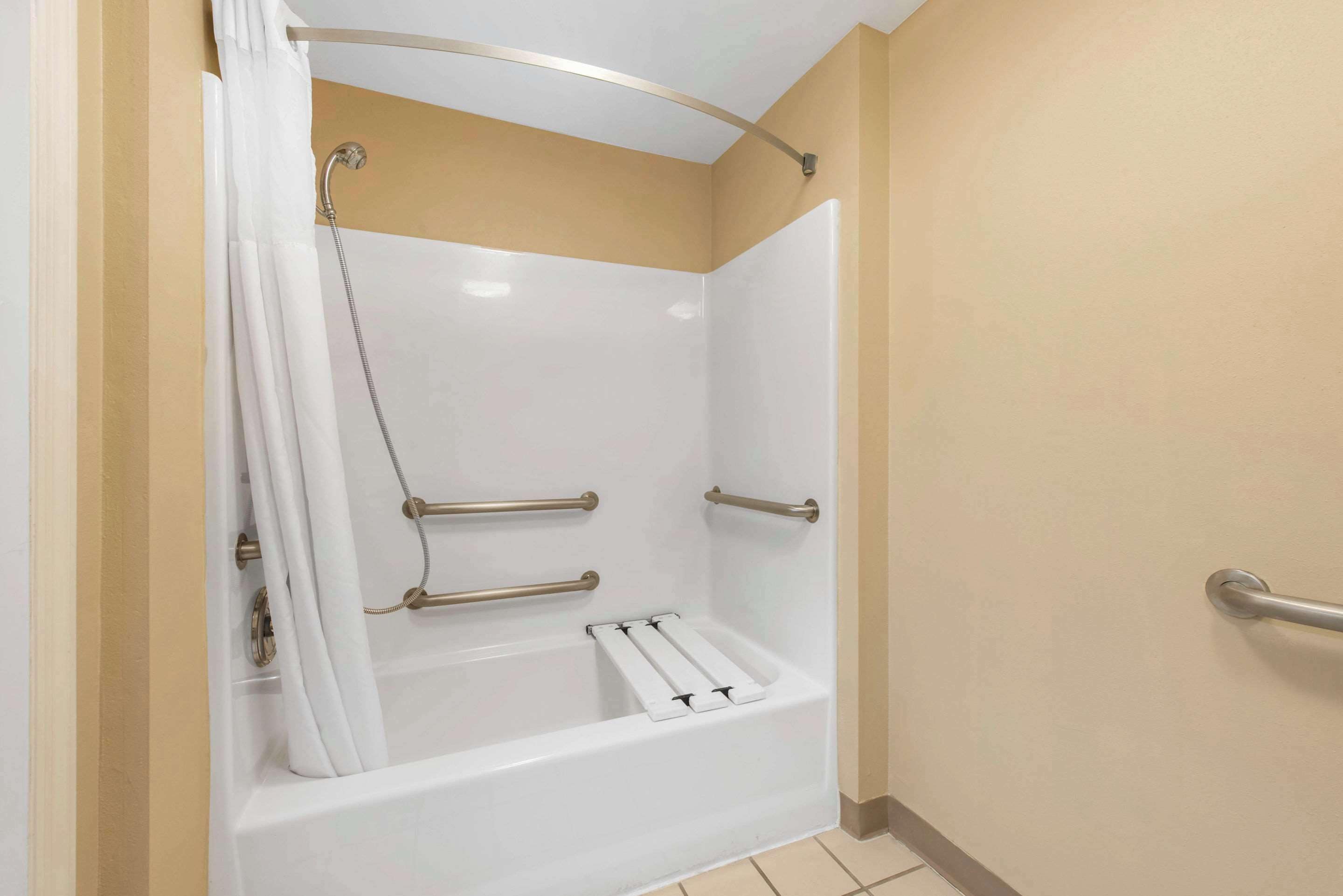 A bathroom with a white bathtub, grab bars, and a shower curtain.