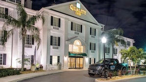 A large, white building with a "Quality Inn" sign, a well-lit entrance, and a black truck parked in front. - Quality Inn Palm Bay - Melbourne I-95 (Palm Bay)