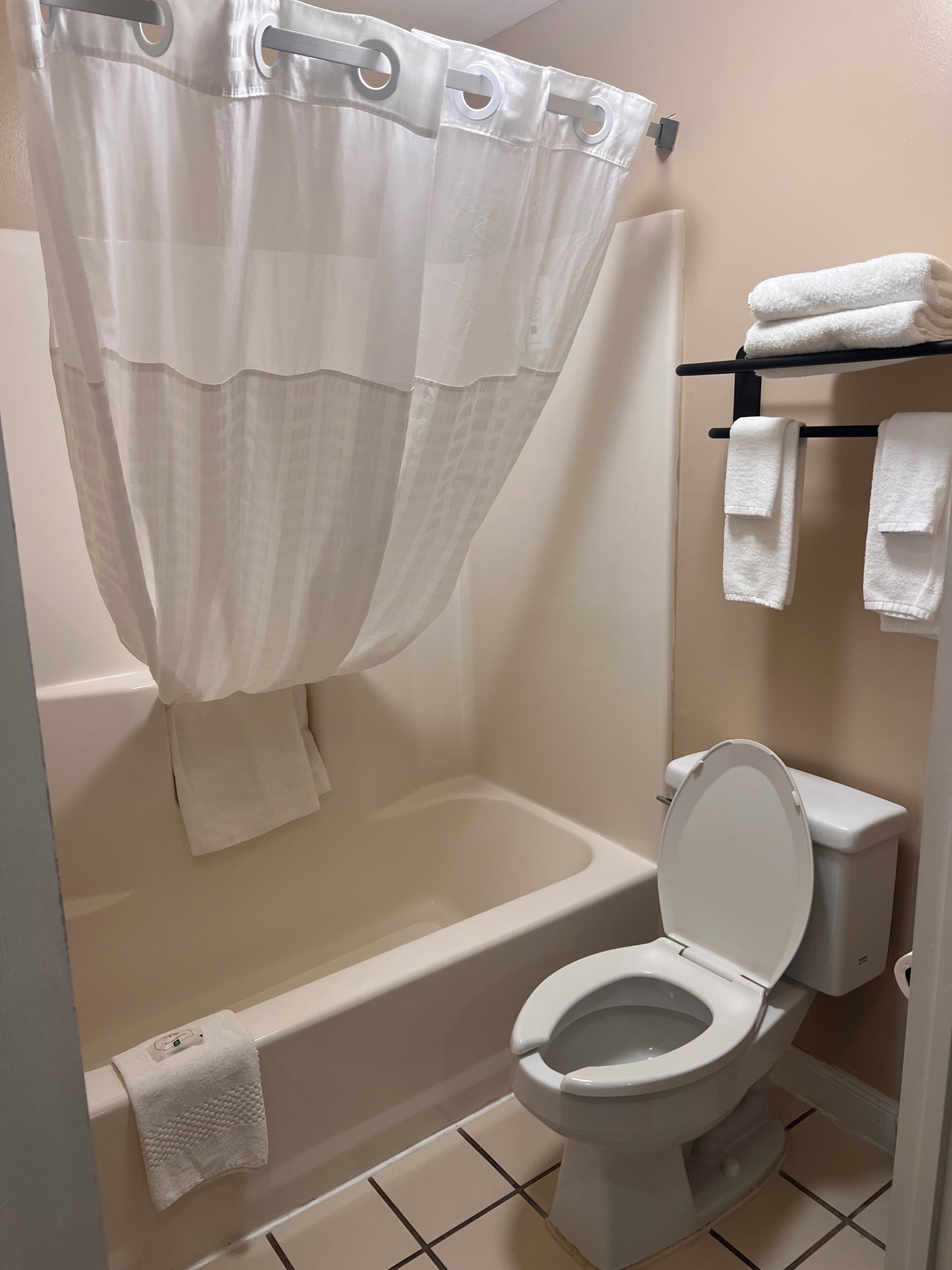 Et badeværelse med badekar, toilet og et håndklædestativ med foldede håndklæder.