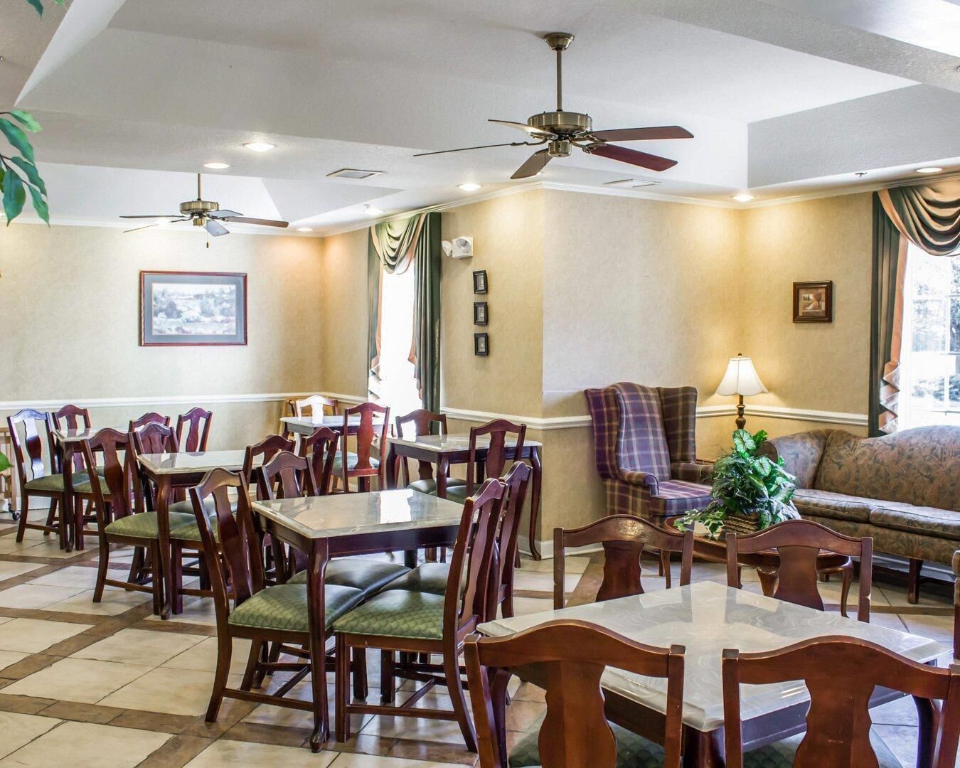 A dining area with multiple tables and chairs, ceiling fans, and a sofa with a lamp.