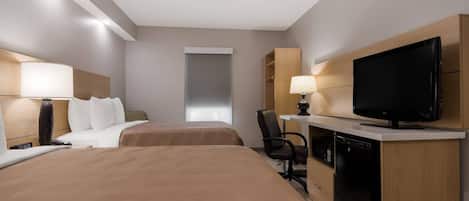 A hotel room with two beds, a desk with a television, a chair, and a small kitchenette.