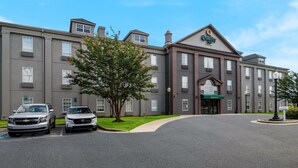 A multi-story hotel with a central entrance, parking spaces, and a tree in front. - Quality Inn Goldsboro (Goldsboro)