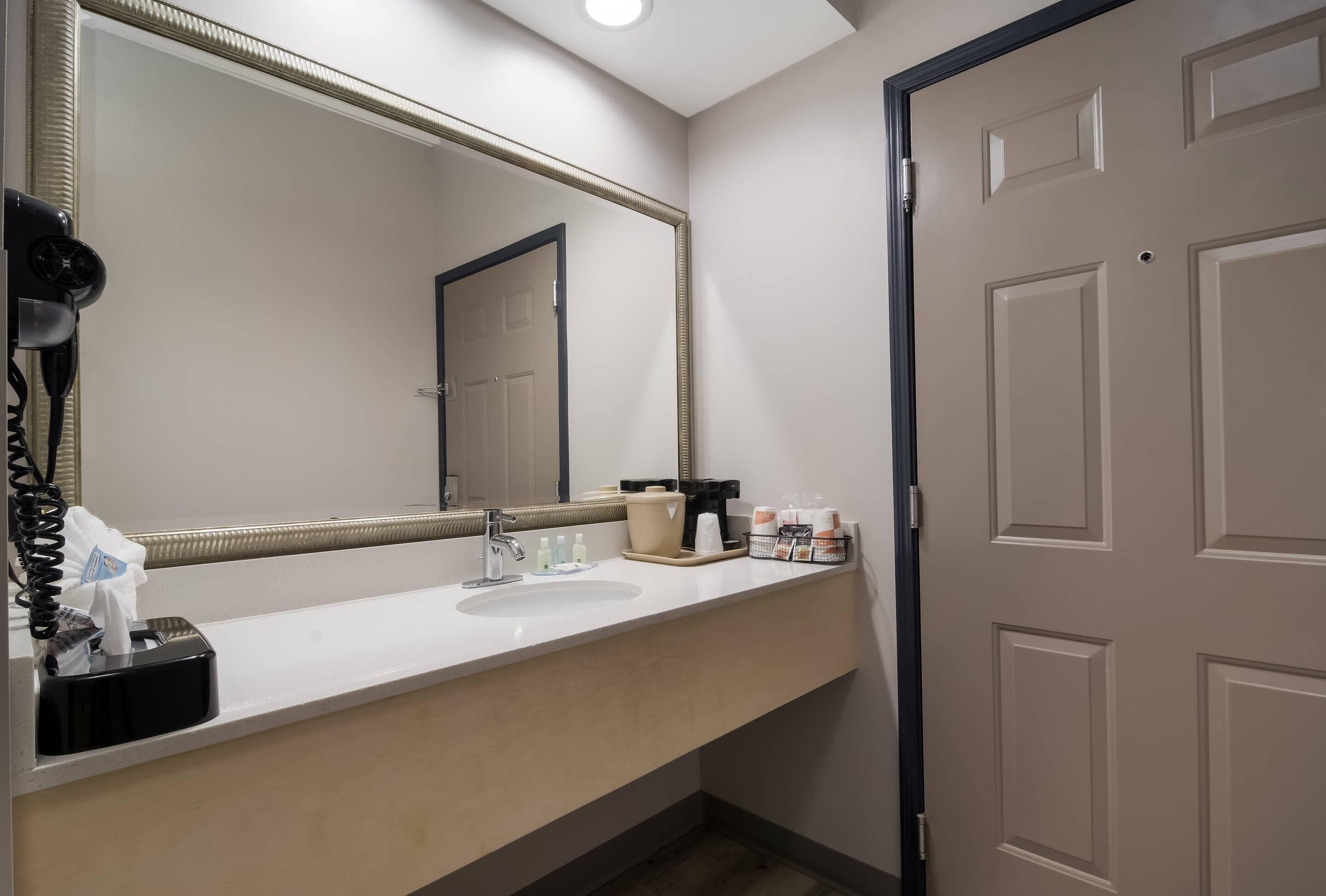 A hotel bathroom with a large mirror, a sink, a hairdryer, and toiletries on the counter.