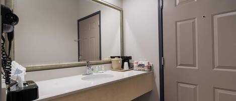 A hotel bathroom with a large mirror, a sink, a hairdryer, and toiletries on the counter.