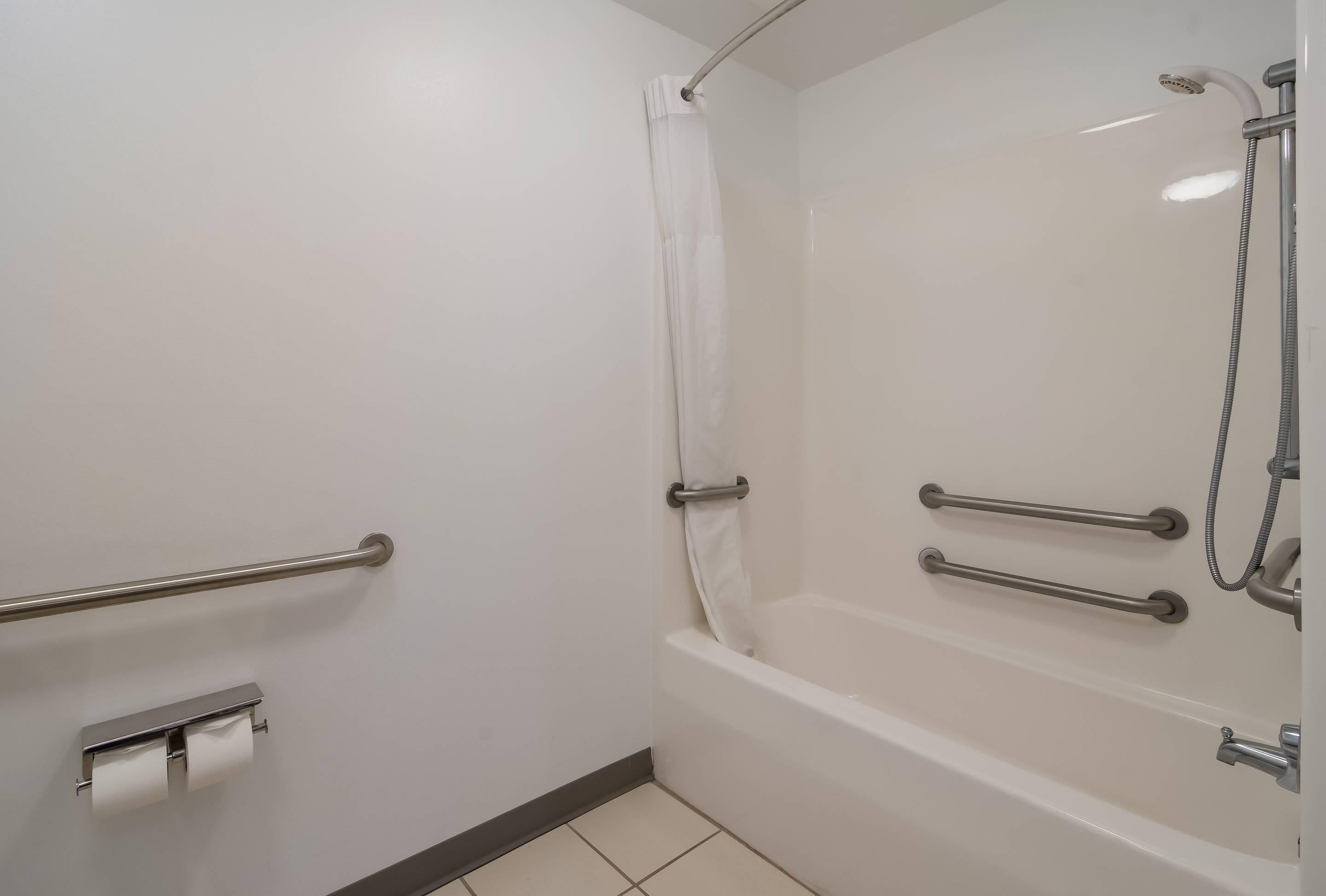 Een badkamer met douche, toilet en handgrepen.