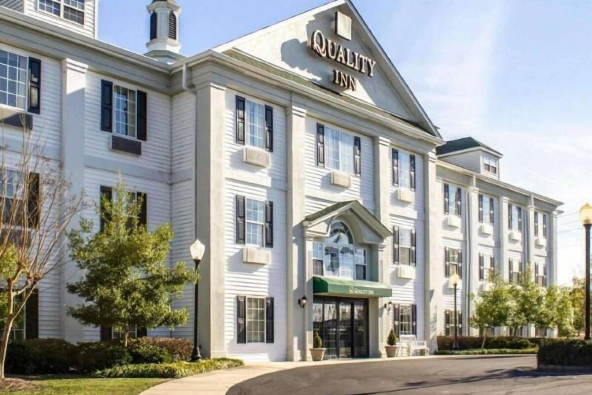 A large, multi-story building with a prominent 'Quality Inn' sign, a central entrance with a green awning, and a symmetrical facade with evenly spaced windows.