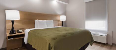 A hotel room with a bed, bedside lamps, a nightstand, a window with blinds, and an air conditioning unit.