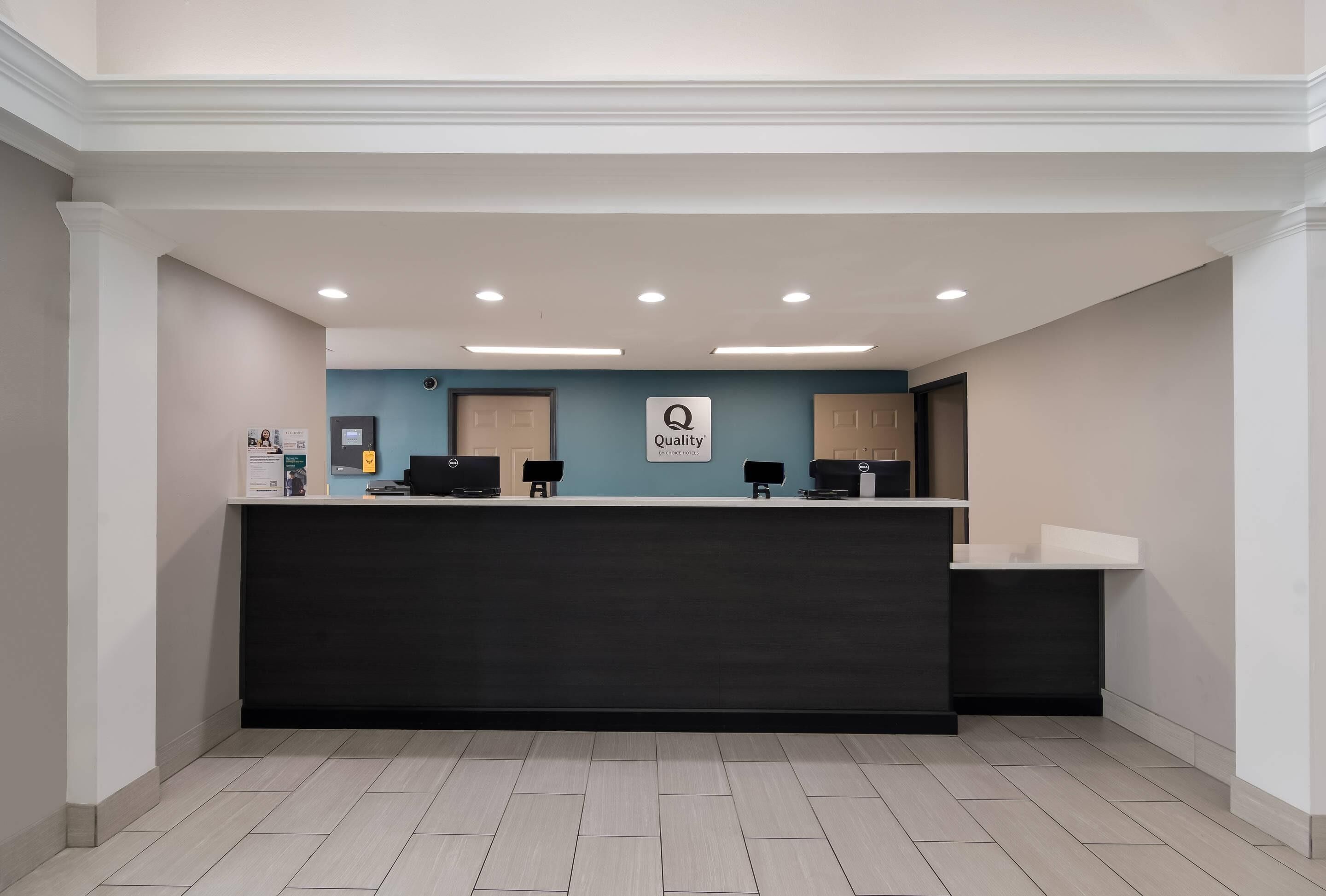 A reception desk with a dark counter, a sign reading 'Quality,' and three computer monitors.