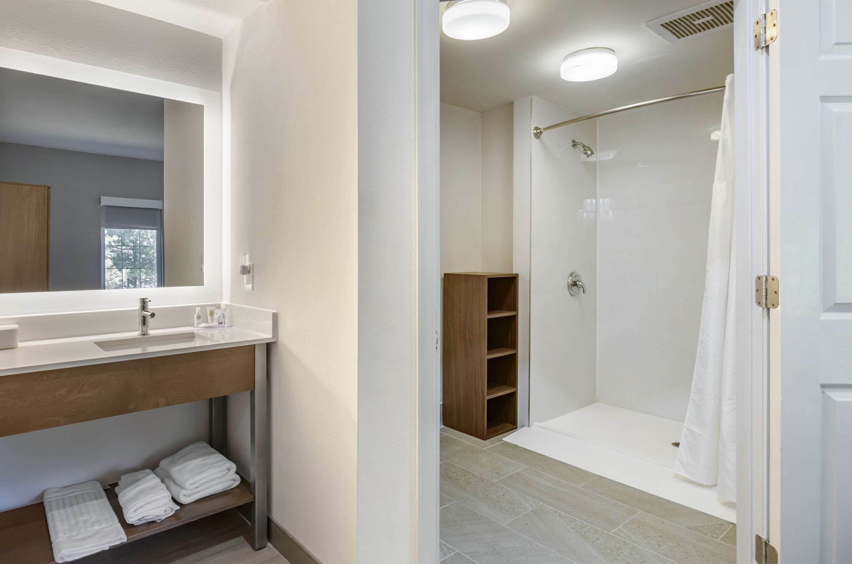 Une salle de bain avec un grand miroir, un lavabo, un espace douche et une étagère en bois.