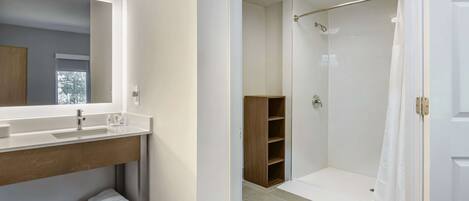 Une salle de bain avec un grand miroir, un lavabo, un espace douche et une étagère en bois.
