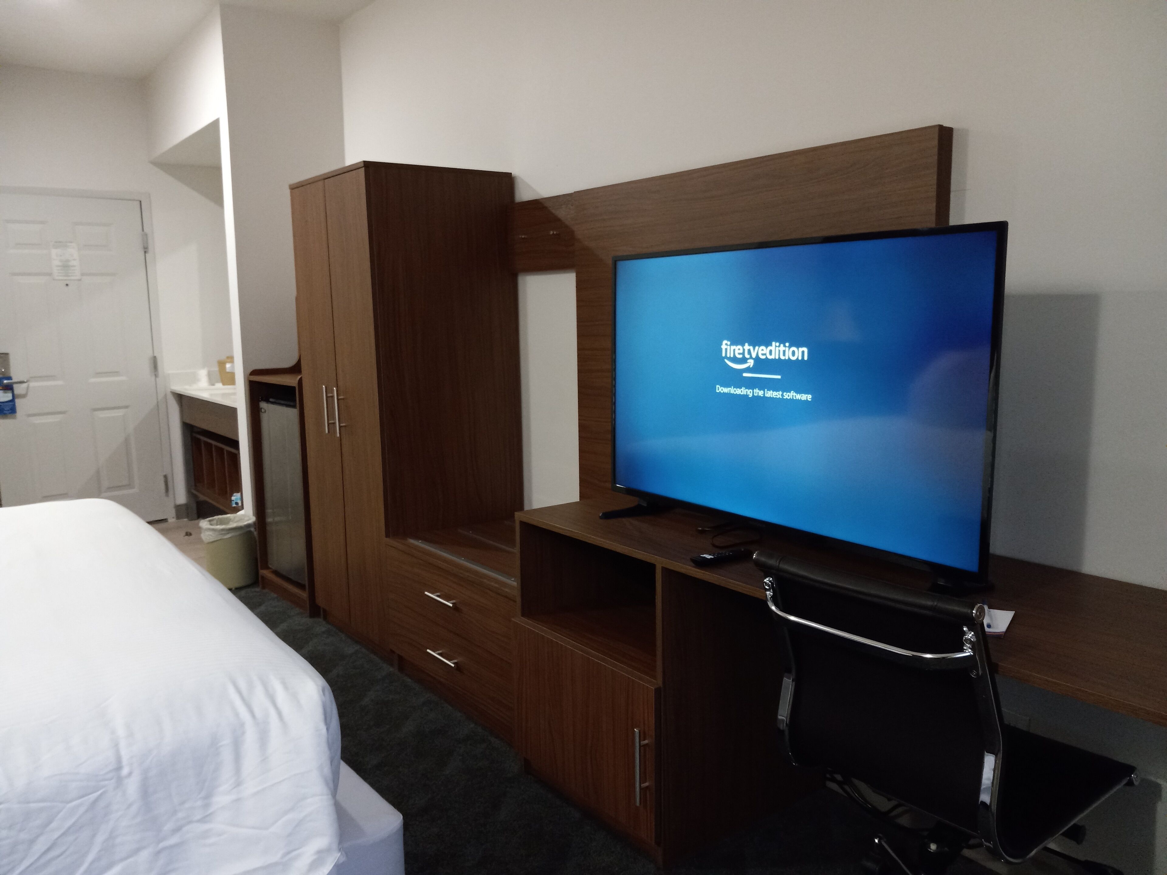 Una habitación de hotel con cama, armario de madera, televisor sobre un mueble bajo y escritorio con silla.