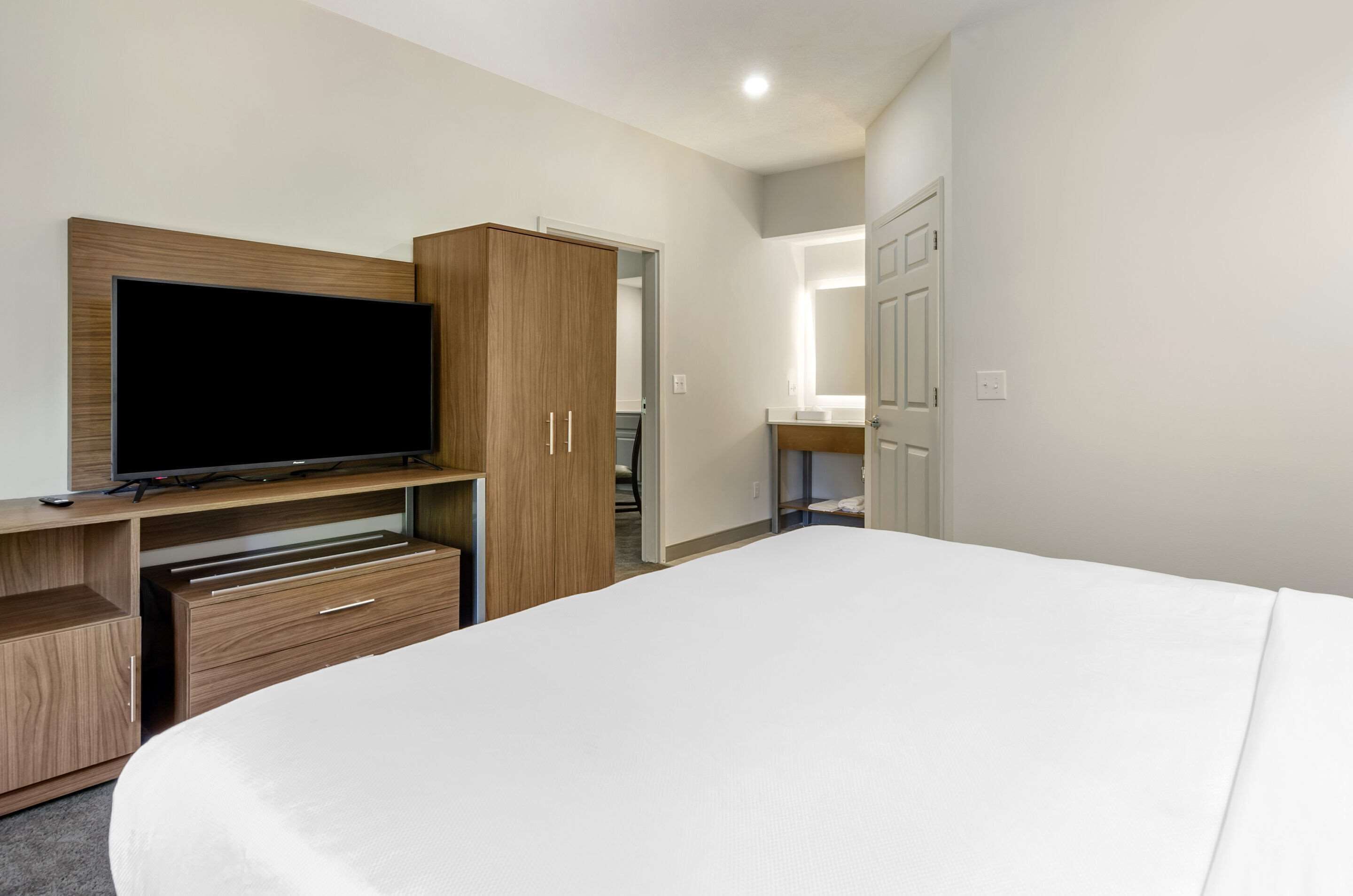 A hotel room with a large bed, a TV on a wooden stand, a wardrobe, and a bathroom visible through an open door.