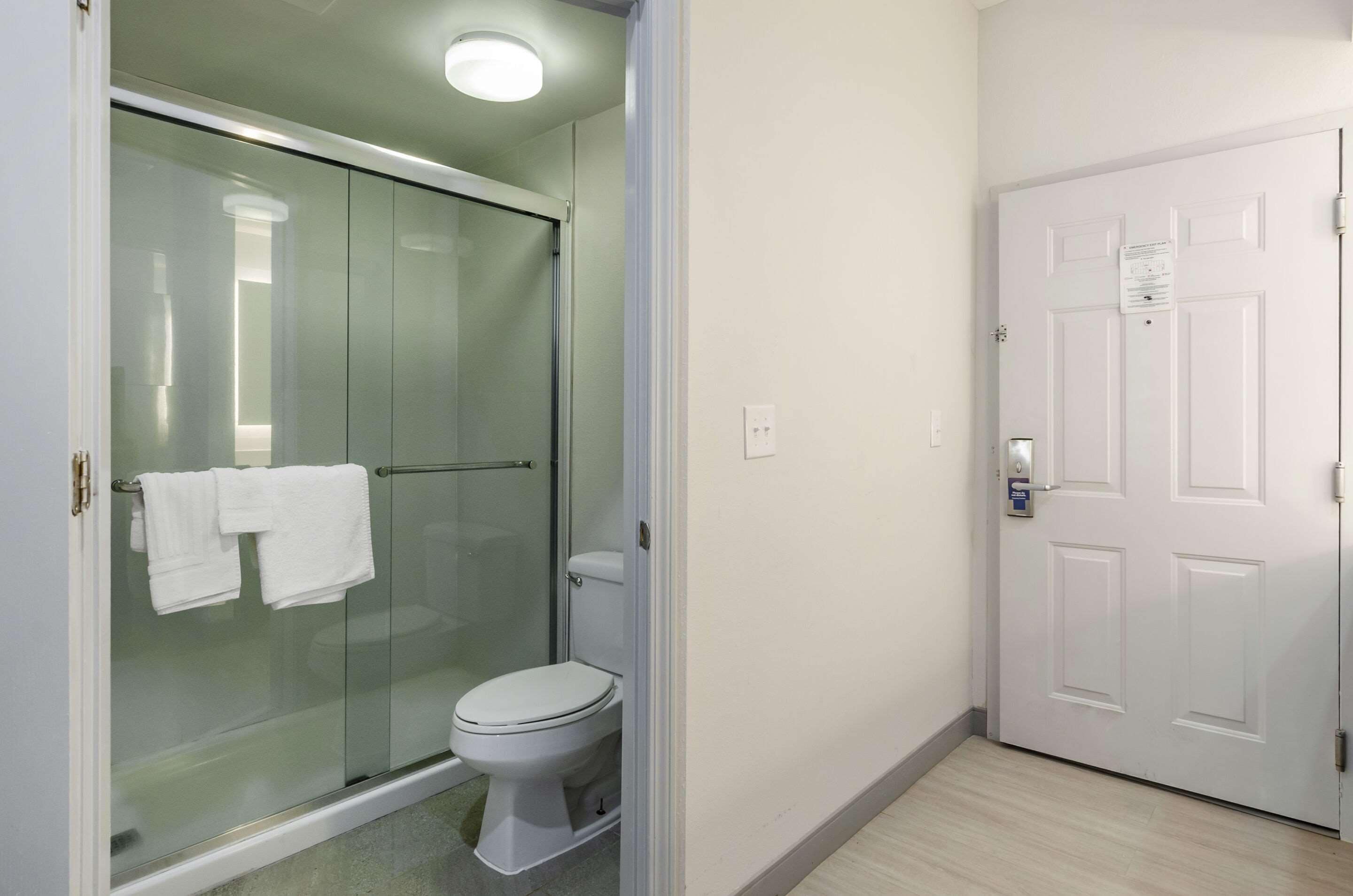 A bathroom with a glass-enclosed shower, a toilet, and a white door with a lock.