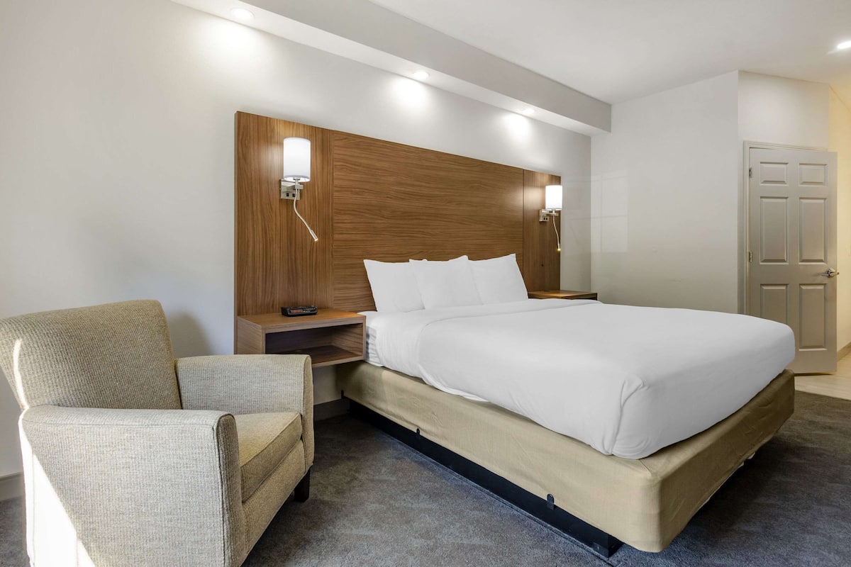 A hotel room with a bed, a chair, a nightstand, and a wooden headboard.