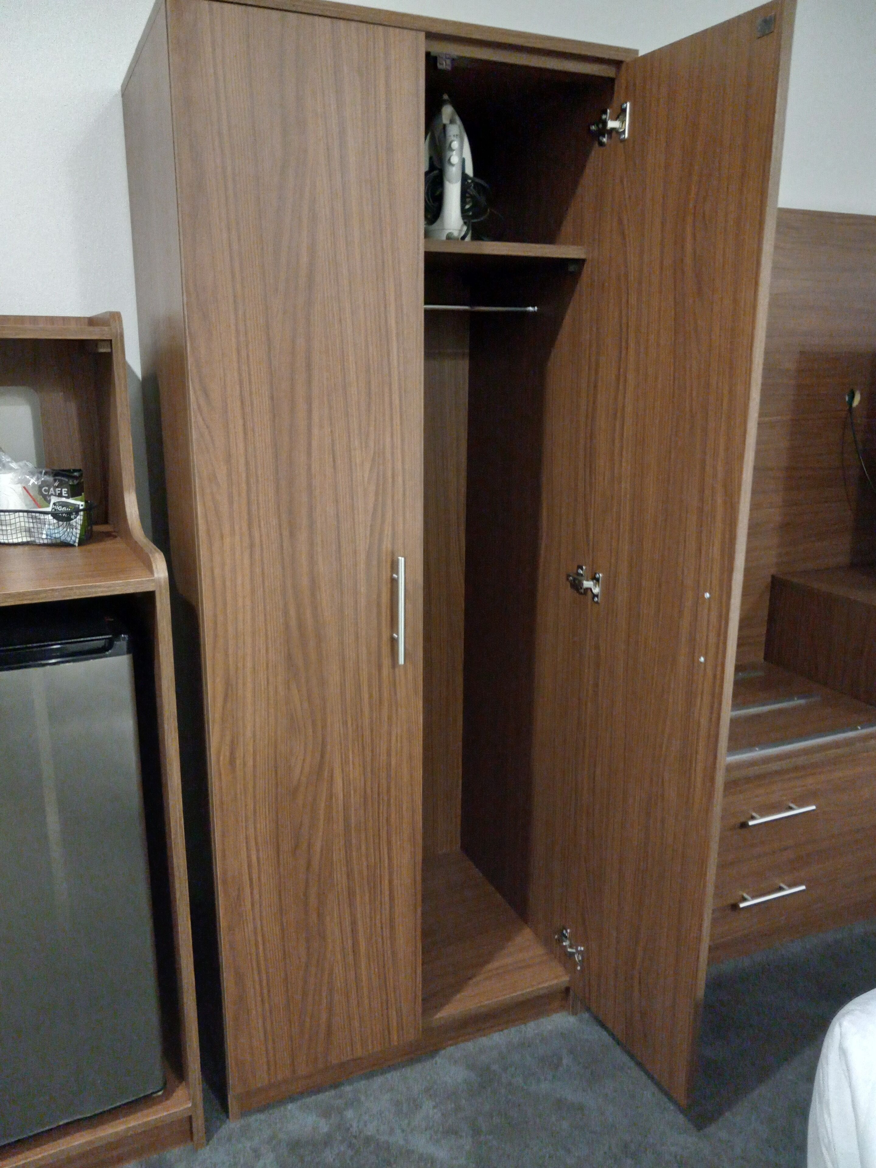 A wooden wardrobe with a small shelf and a drawer, a compact refrigerator, and a staircase leading to an upper level.