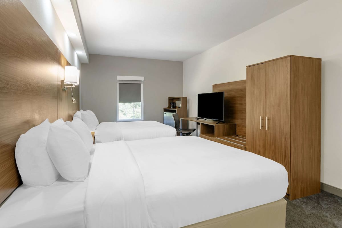 A modern hotel room with two beds, a TV, a wardrobe, and a coffee machine.