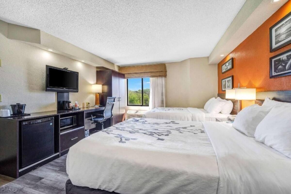 A hotel room with a bed, desk, television, and a window with curtains.