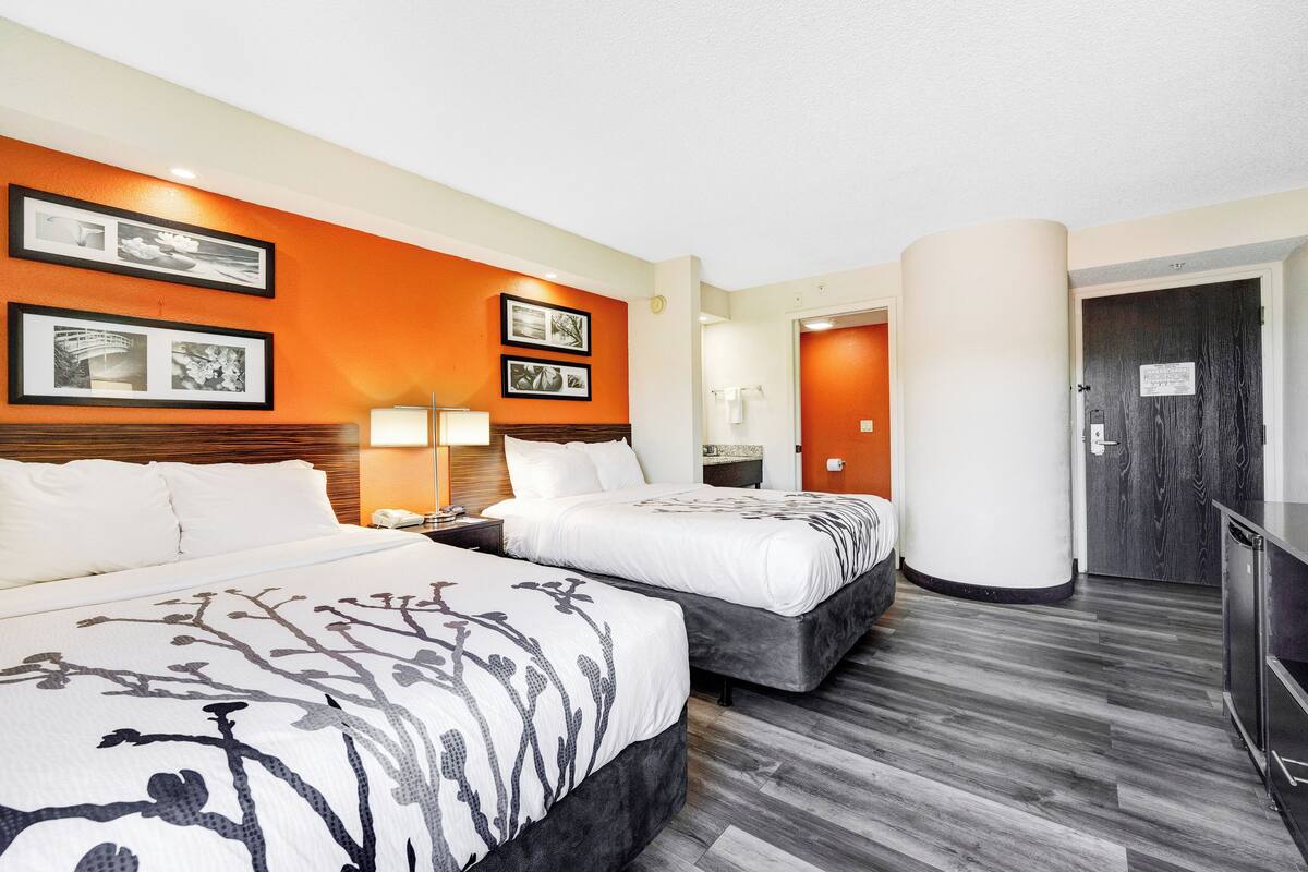 A hotel room with two beds, a wooden headboard, a nightstand with a lamp, and a large pillar.
