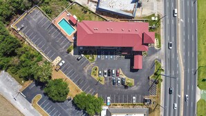 Vista aérea de un edificio con techo rojo, piscina y aparcamiento con varios coches.