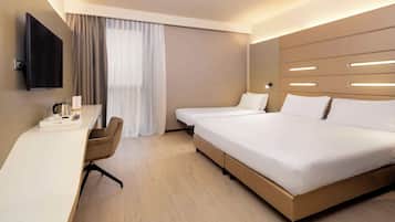 Een moderne hotelkamer met een bureau, twee bedden, een televisie en een groot raam met gordijnen.