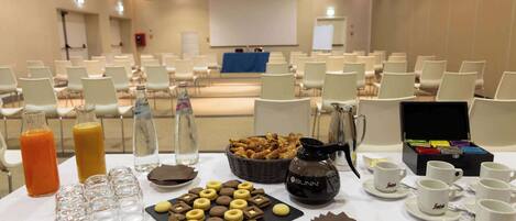 A conference room with rows of chairs, a projector screen, and a buffet table with snacks and drinks.
