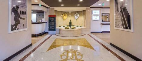 A hotel lobby with a reception desk, a large emblem on the floor, and framed artwork on the walls.