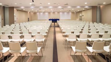 A conference room with rows of white chairs, a blue table at the front, and beige carpet.