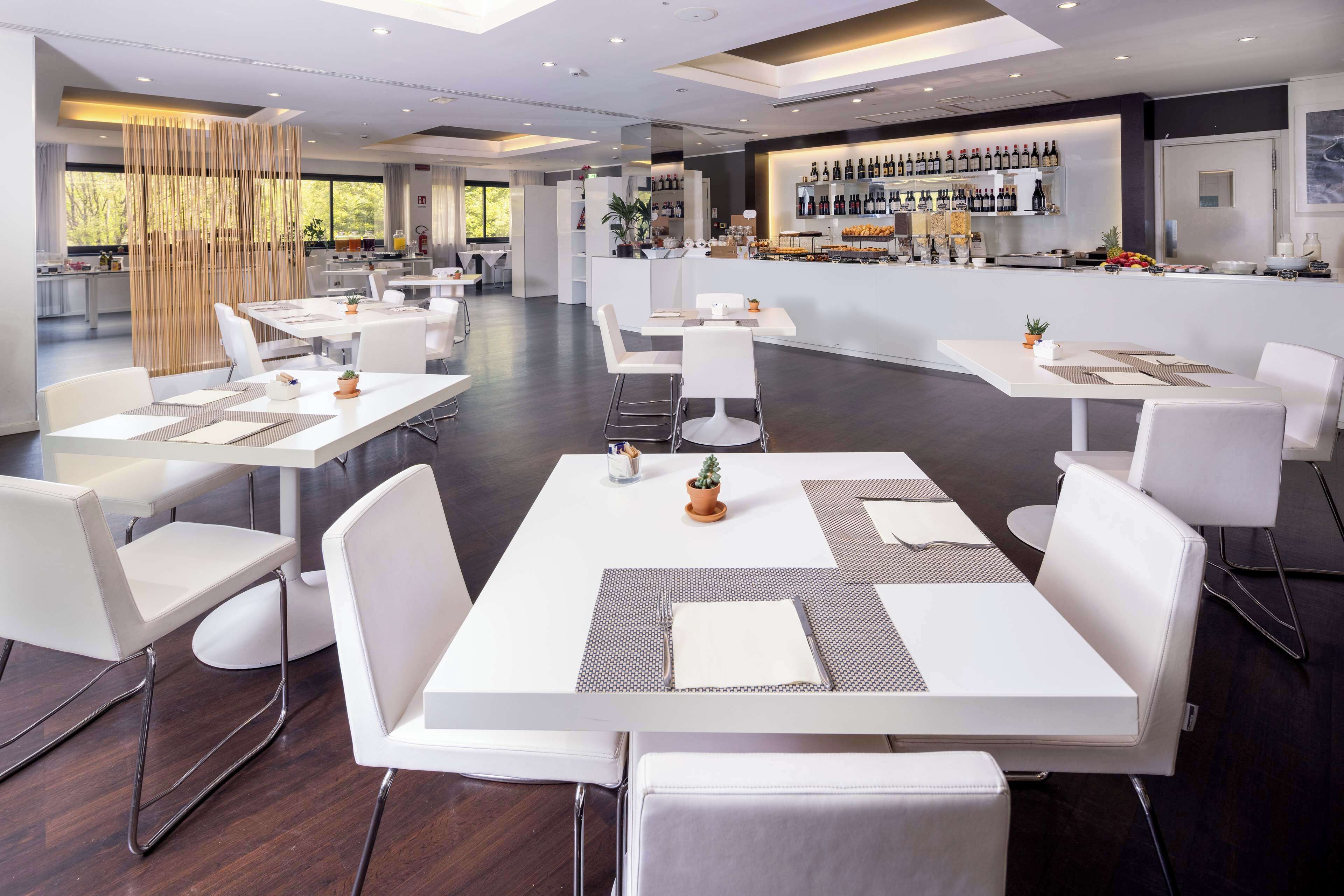 En moderne restaurant med hvide borde og stole, et barområde med et udvalg af vin, og udsigt til det fri.