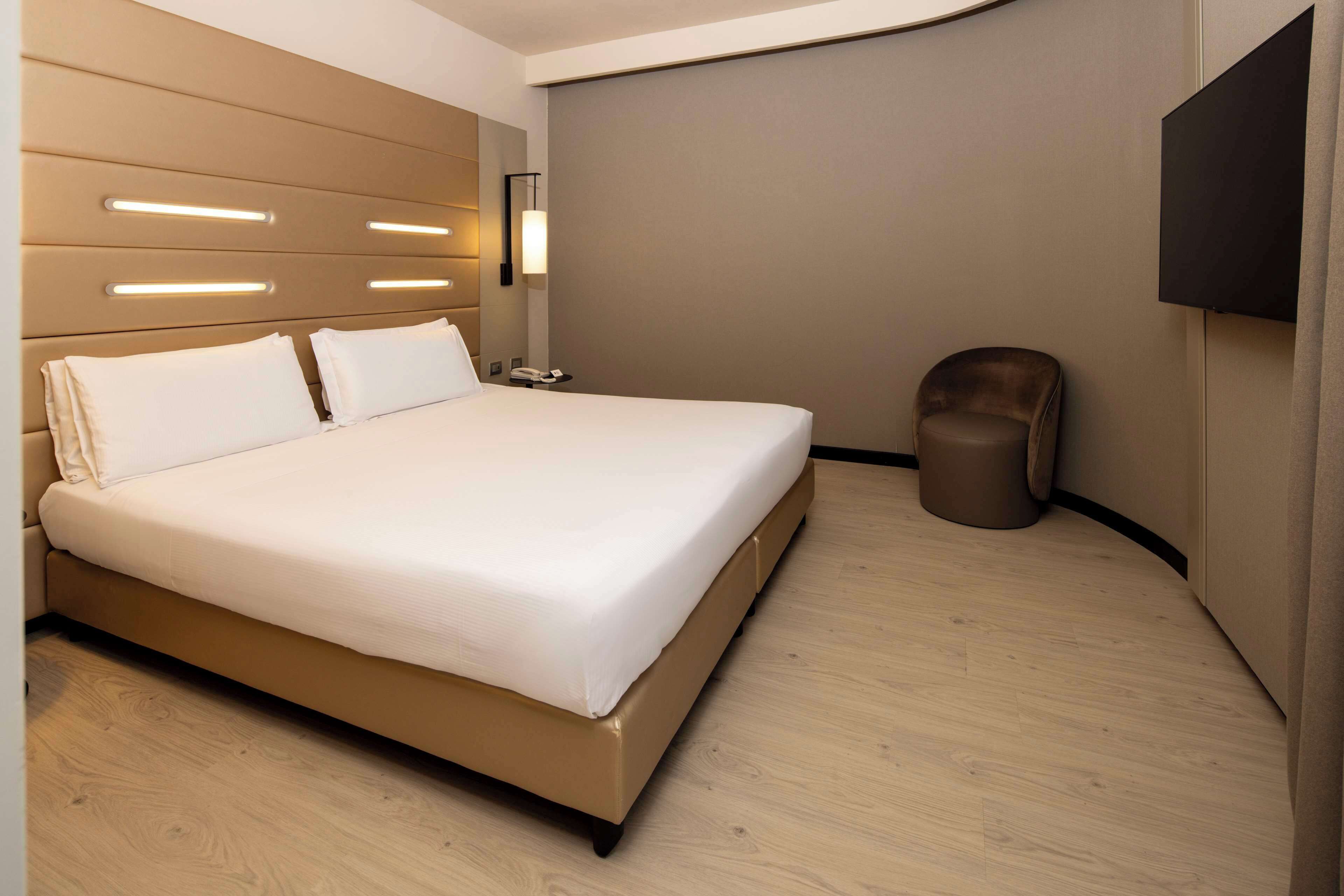 A modern hotel room with a large bed, bedside tables, a flat-screen TV, and a waste bin.