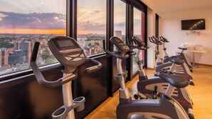 A gym with cardio machines and a city view through large windows. - Best Western Plus Tower Hotel Bologna (Bologna)