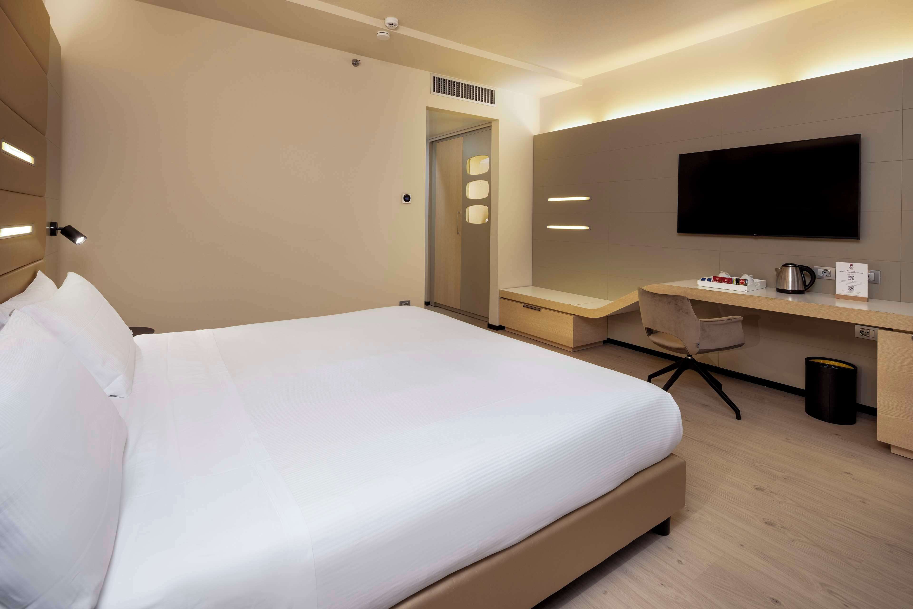 A modern hotel room with a large bed, a desk with a flat-screen TV, and a coffee maker.