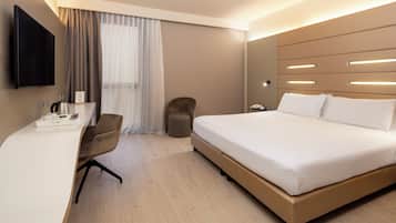 Una camera d'albergo moderna con un letto grande, una scrivania con una TV a schermo piatto, una sedia e uno sgabello.