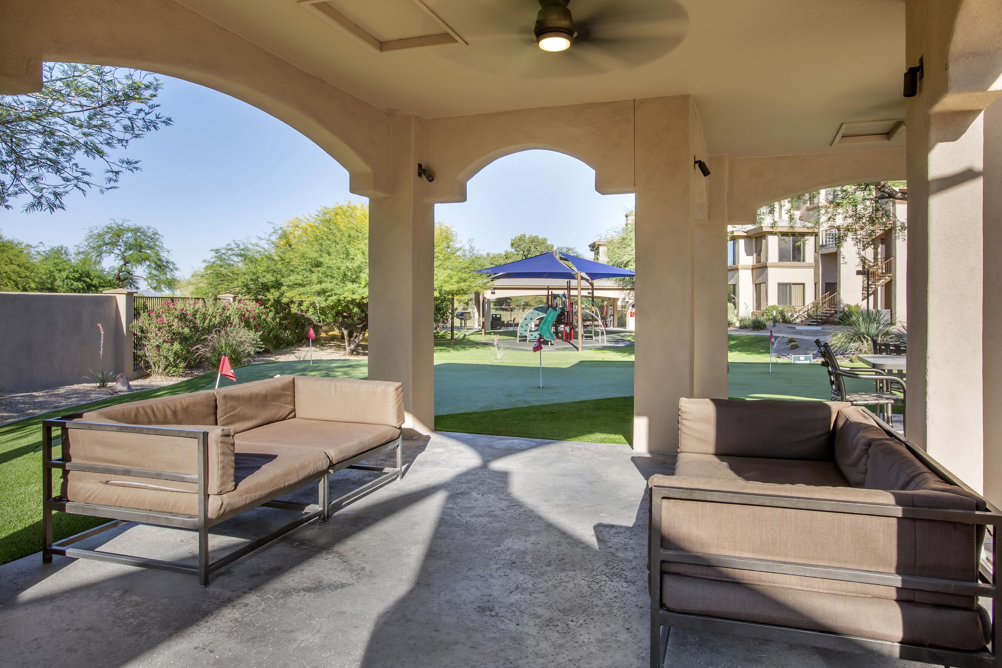 A covered outdoor seating area with a view of a playground and a building in the background.