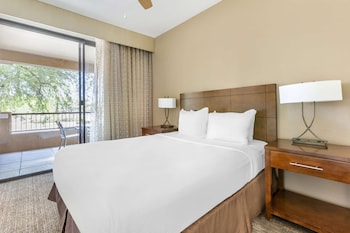 Relax in this serene hotel room with a large bed, two bedside tables, and a balcony offering a view of the surrounding trees. at Hilton Vacation Club Scottsdale Links Resort