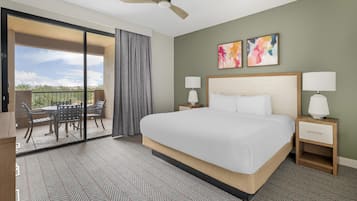 Habitación de hotel con una cama, dos lámparas de noche, un ventilador de techo, un balcón con mesa y sillas, y dos cuadros abstractos en la pared.