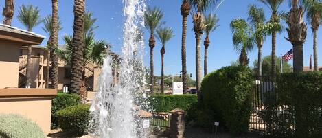 Una fuente rodeada de palmeras y un edificio con un letrero que indica un hotel o resort.
