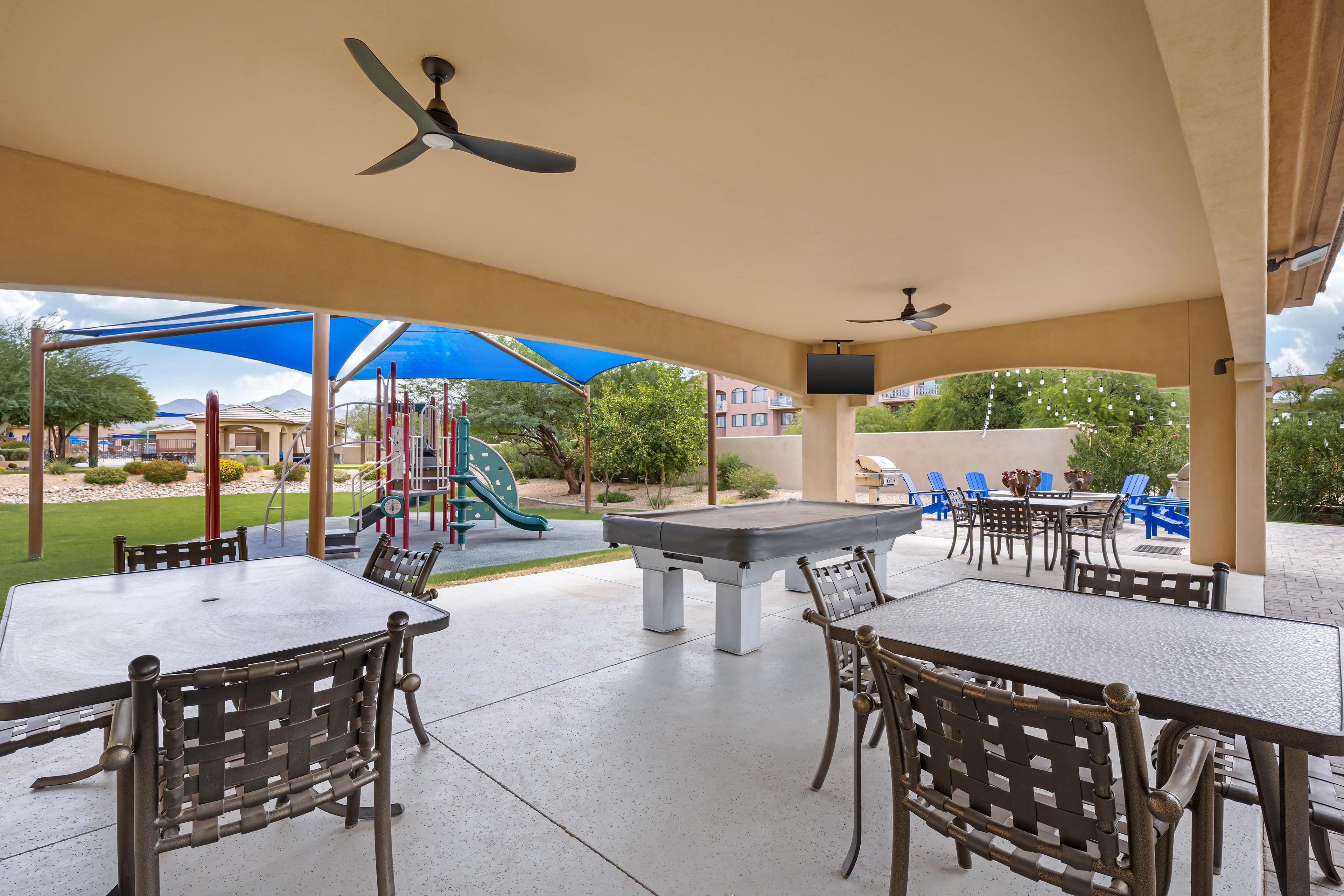 An outdoor patio area with tables and chairs, a pool table, and a children's play structure.
