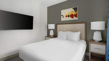 A hotel room with a bed, two bedside tables with lamps, a flat-screen TV mounted on the wall, and a painting above the bed.
