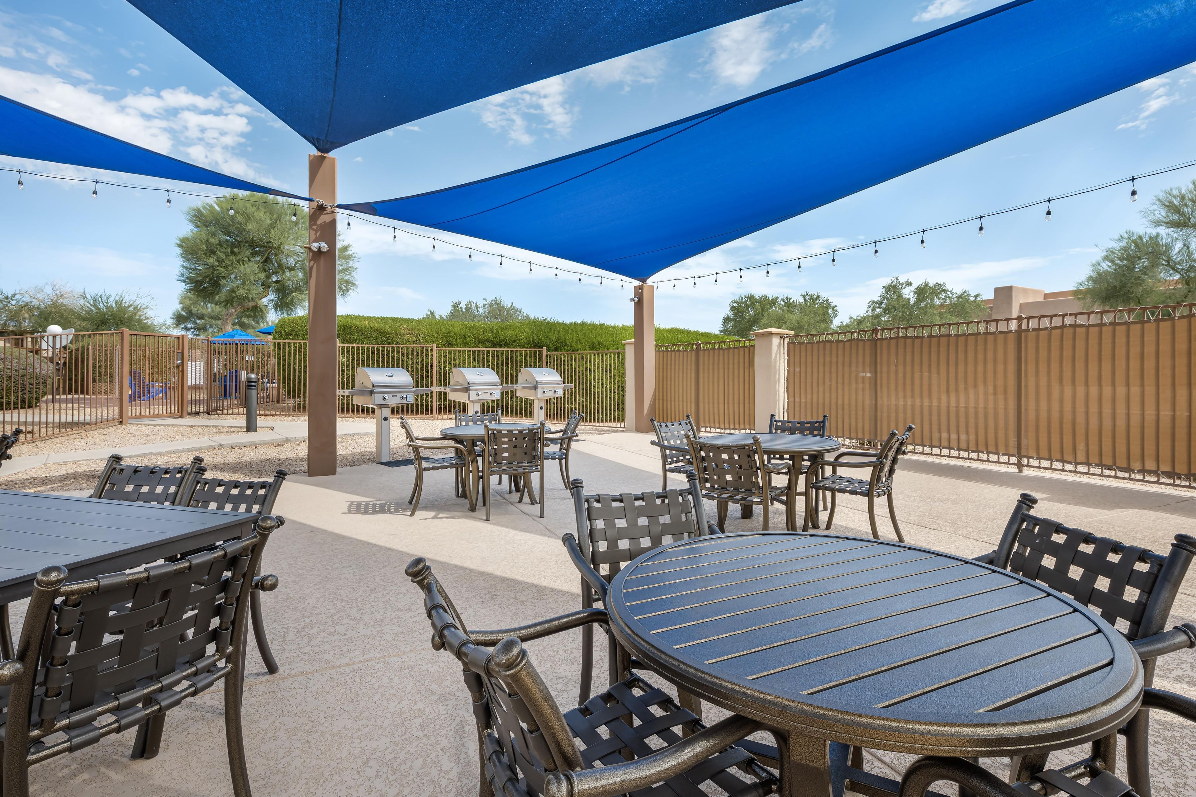 An outdoor patio area with round tables and chairs, a barbecue grill, and string lights.